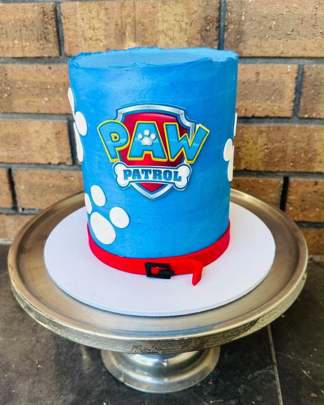 Blue Paw Patrol birthday cake with edible logo, white paw prints and red fondant belt detail
